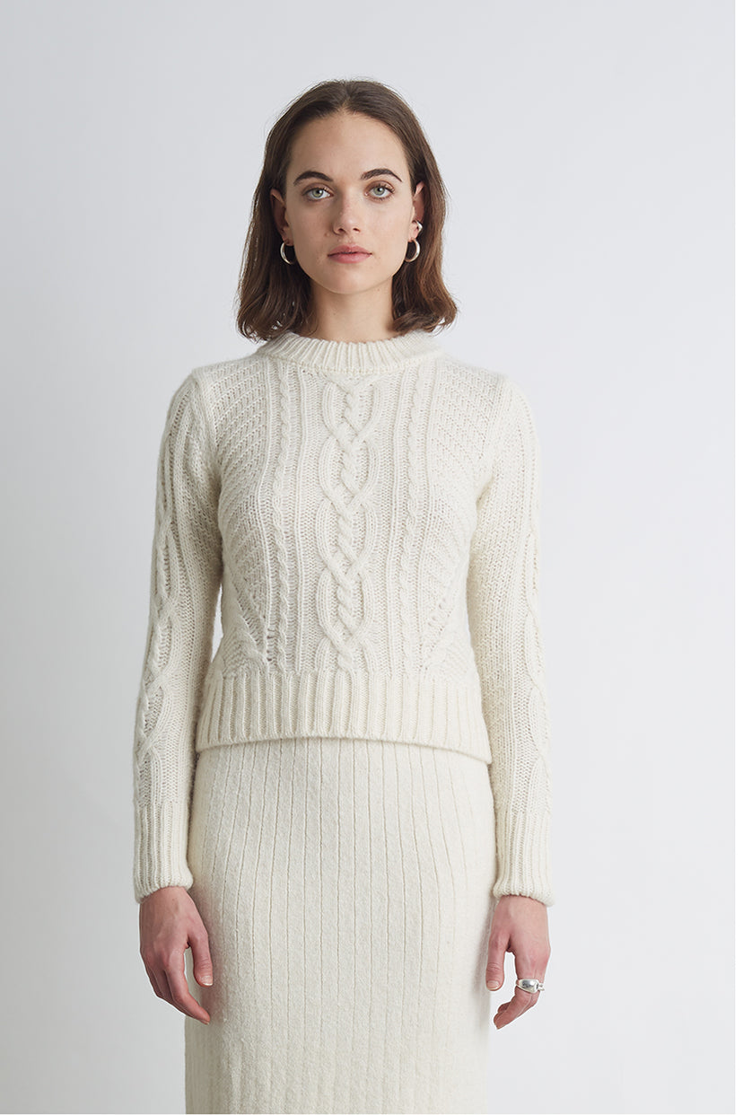 Woman in a cream cable-knit sweater with a midi skirt